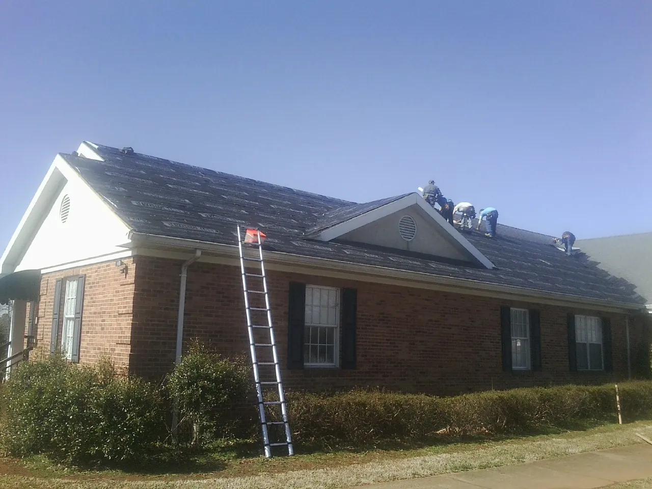 Crew tearing shingles off a brick ranch roof with a ladder set — Metal Roof Repair work by our crew in Enon Valley