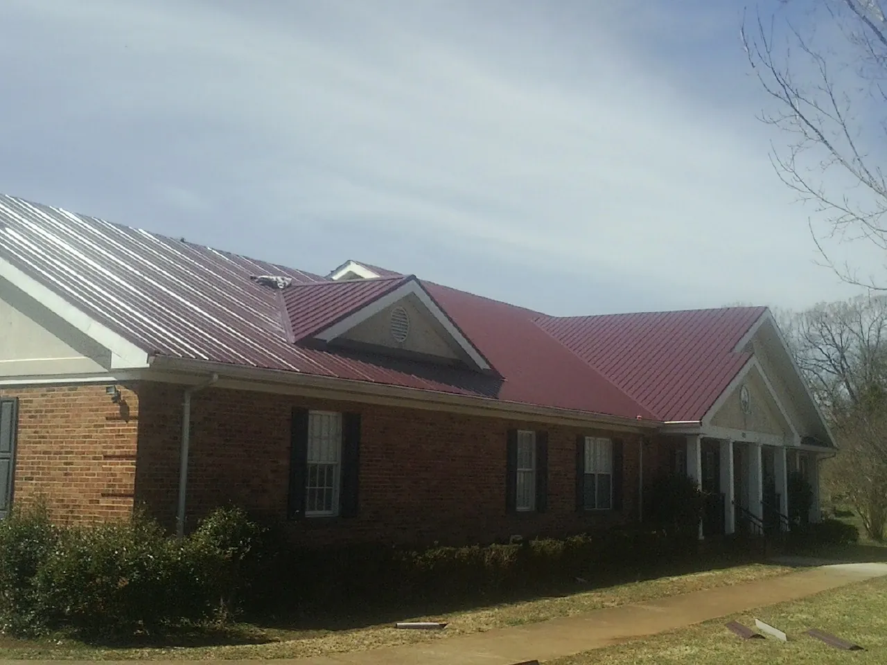 Red metal roof with gabled entries on a long brick building, from a Hail Damage Roof Repair job in Enon Valley