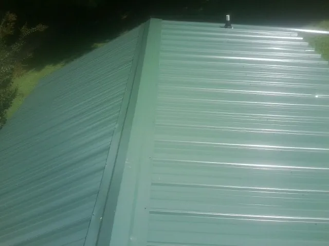 New green metal panels meeting at the ridge of a roof — Flat Roof Repair work by our crew in Enon Valley