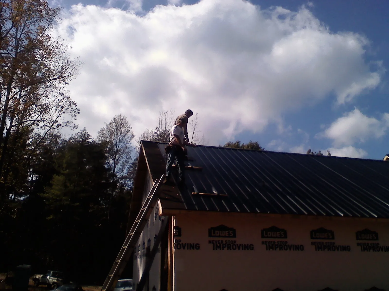 Roofer fastening dark metal panels high against a cloudy sky, from a Roof Inspection job in Enon Valley