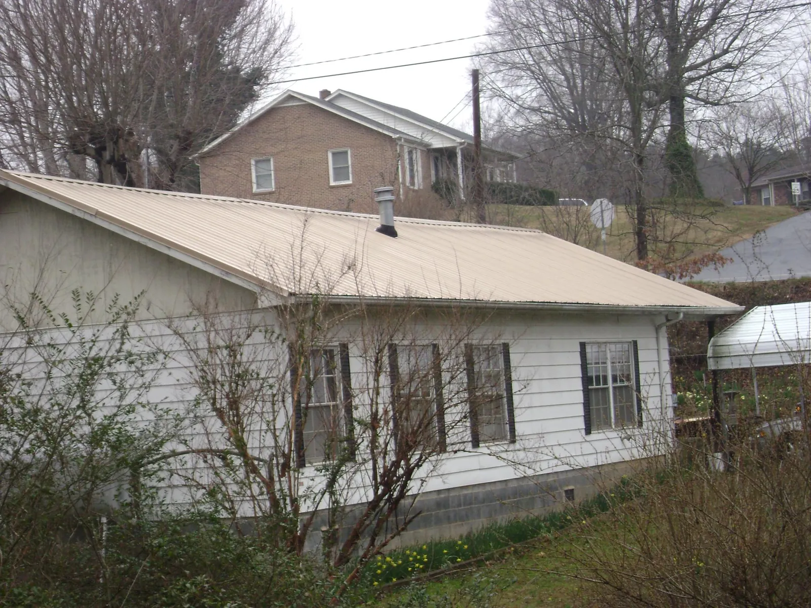 Tan metal roof on a white sided house set into a hillside — Commercial Roofing by Roofing Brothers in Enon Valley